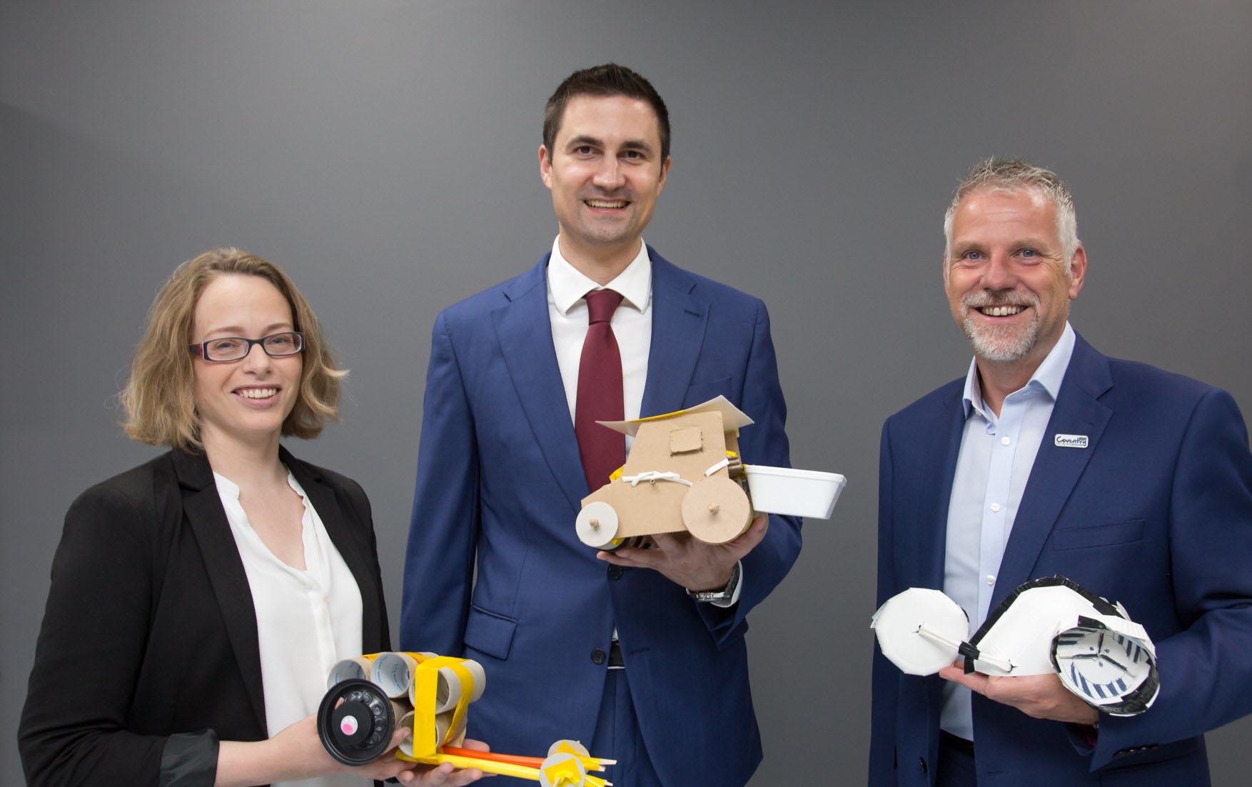 A woman and two men holding model cars made of cardboard and recycled materials.