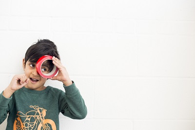 a boy looking through shiny red roll of tape