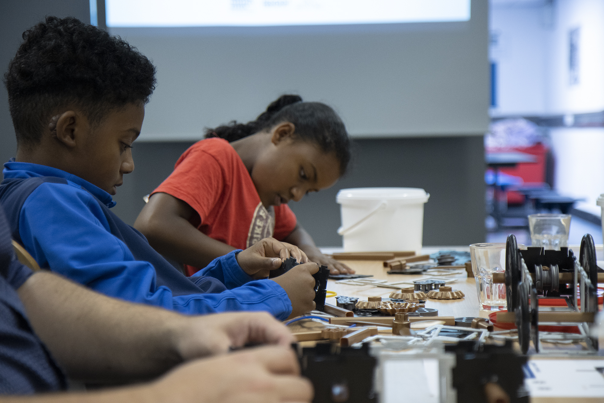 A boy and a girl sitting at a table, creating model vehicles using Polydron construction kits