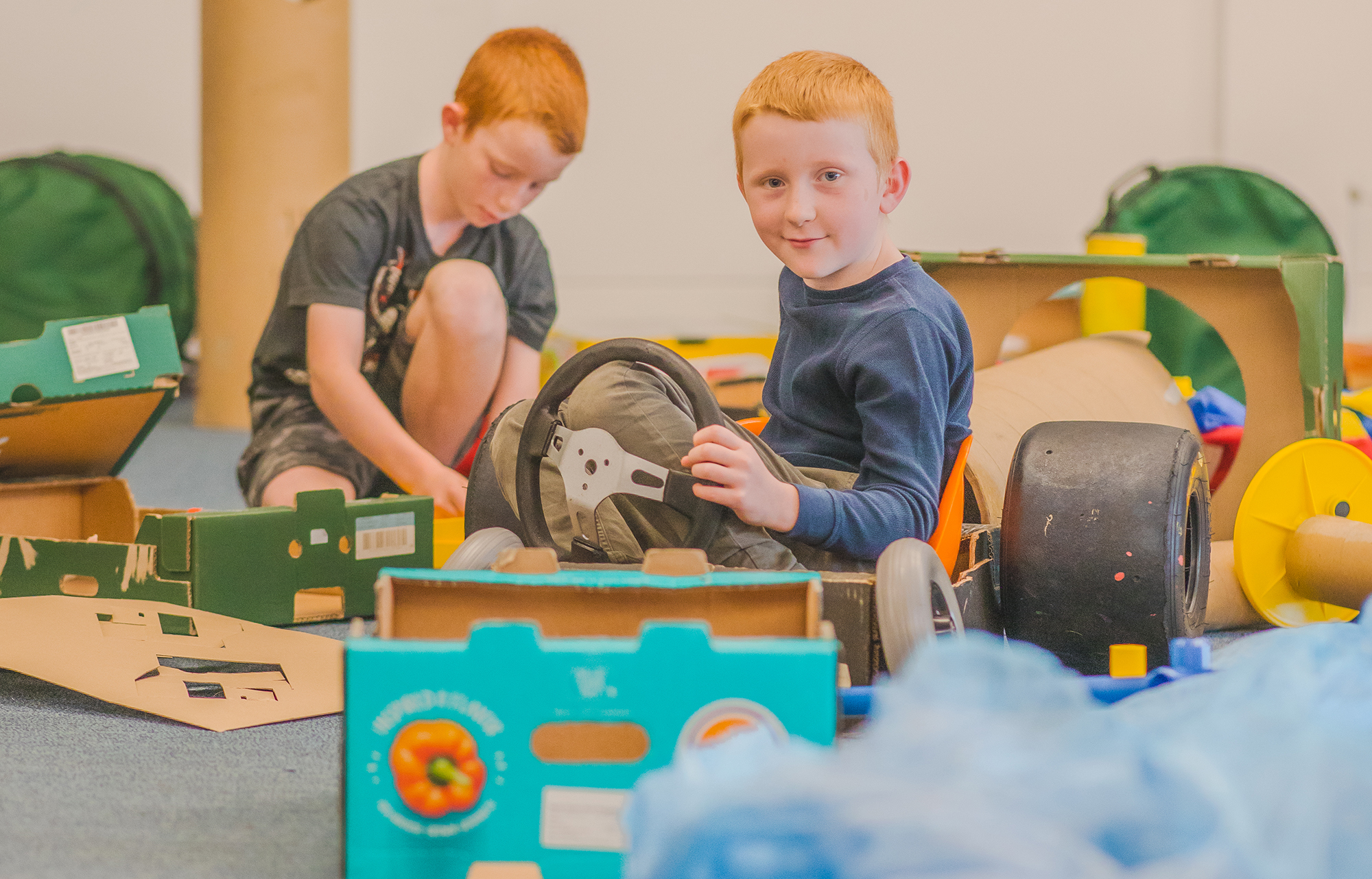 Two boys building a car from cardboard boxes and wheels