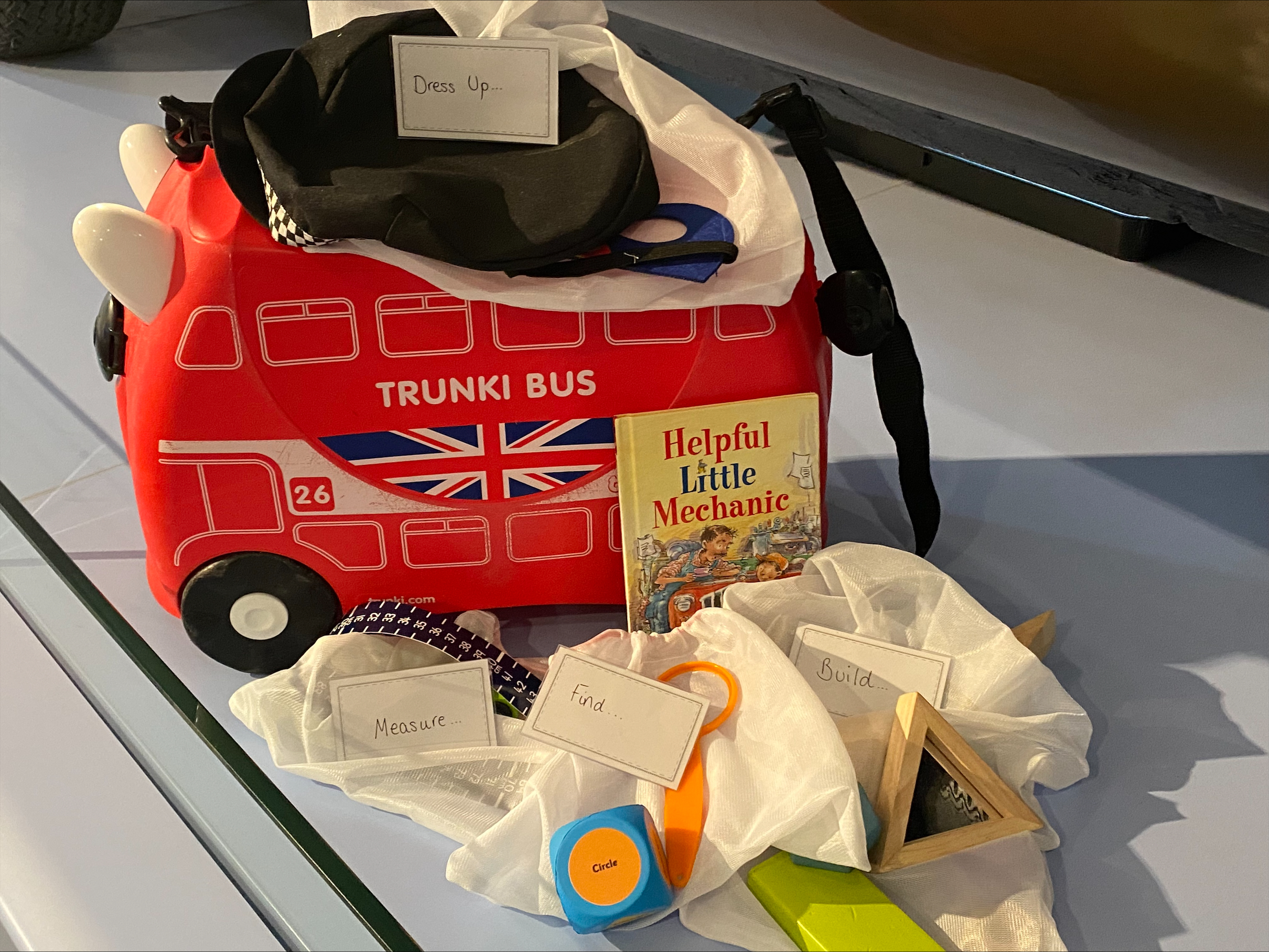 A photograph of a red trail box containing a measuring tape and activity cards