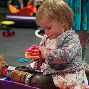 A little girl sitting on the floor holding a set of brightly coloured plastic shapes