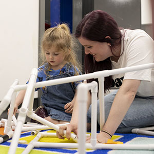 A woman and a little girl are building a structure with white plastic pipes
