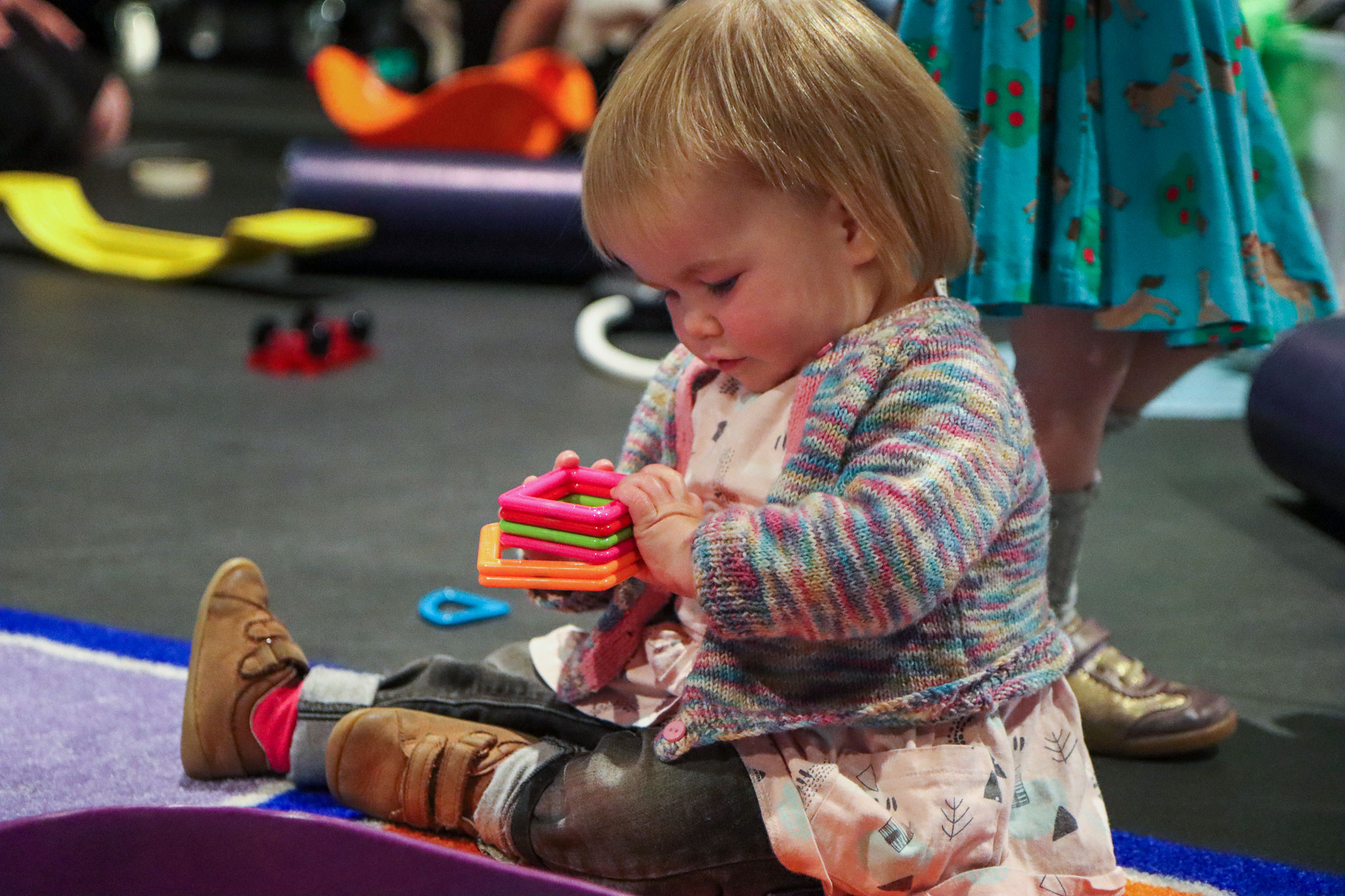A girl sitting on a rug in Coventry Transport Museum, playing with a set of colourful plastic shapes