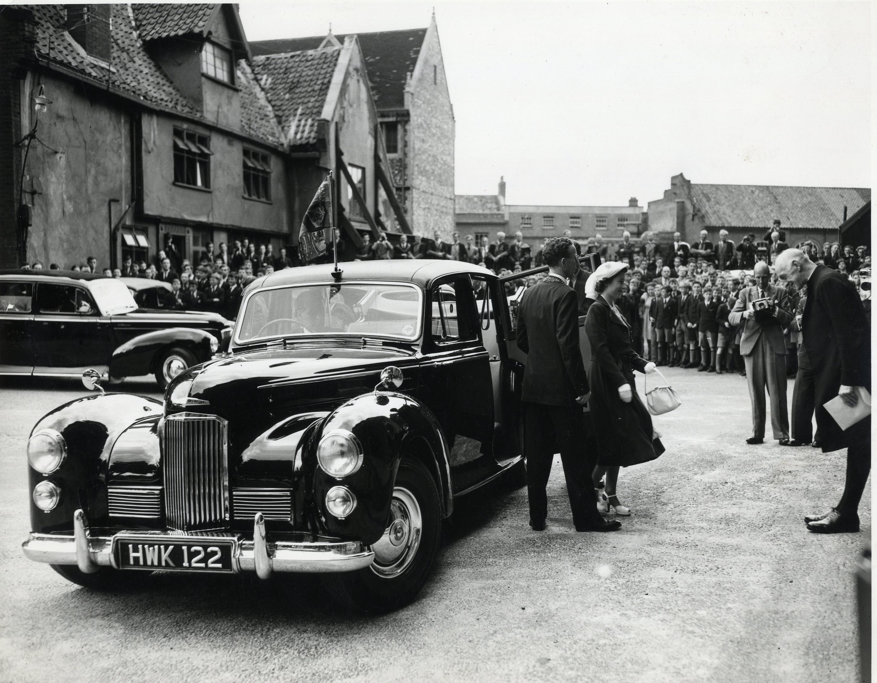 A black and white photograph of the then Princess Elizabeth stepping out of a Coventry car and being greeted by the Lord Bishop in Norwich.