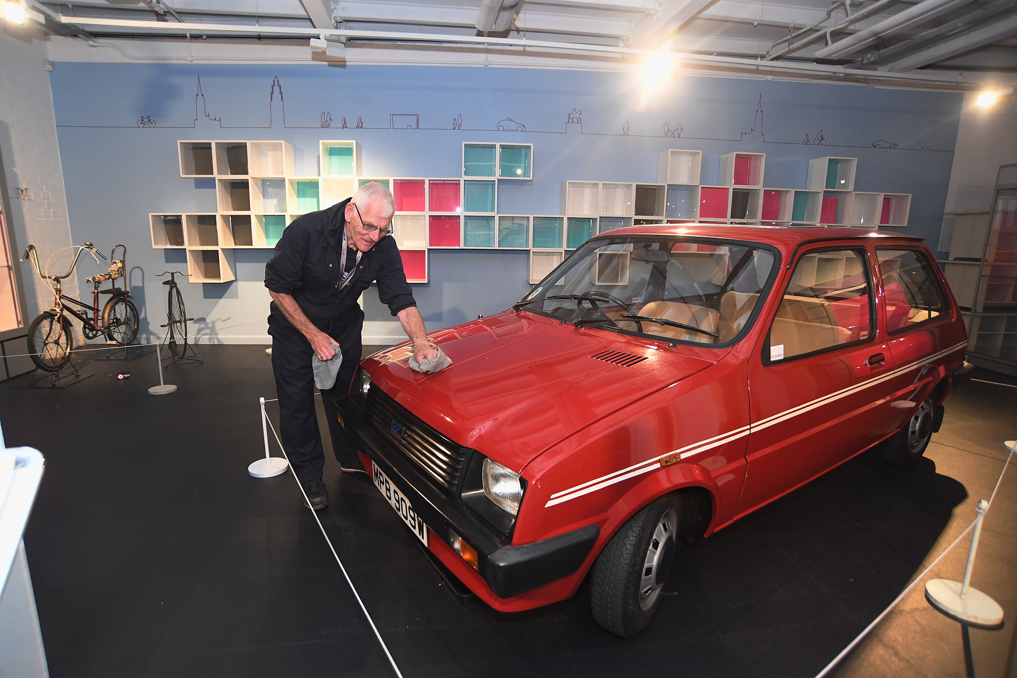 A member of the Coventry Transport Museum workshop team dressed in overalls, polishing Princess Diana's red Austin Mini Metro L on display in the museum