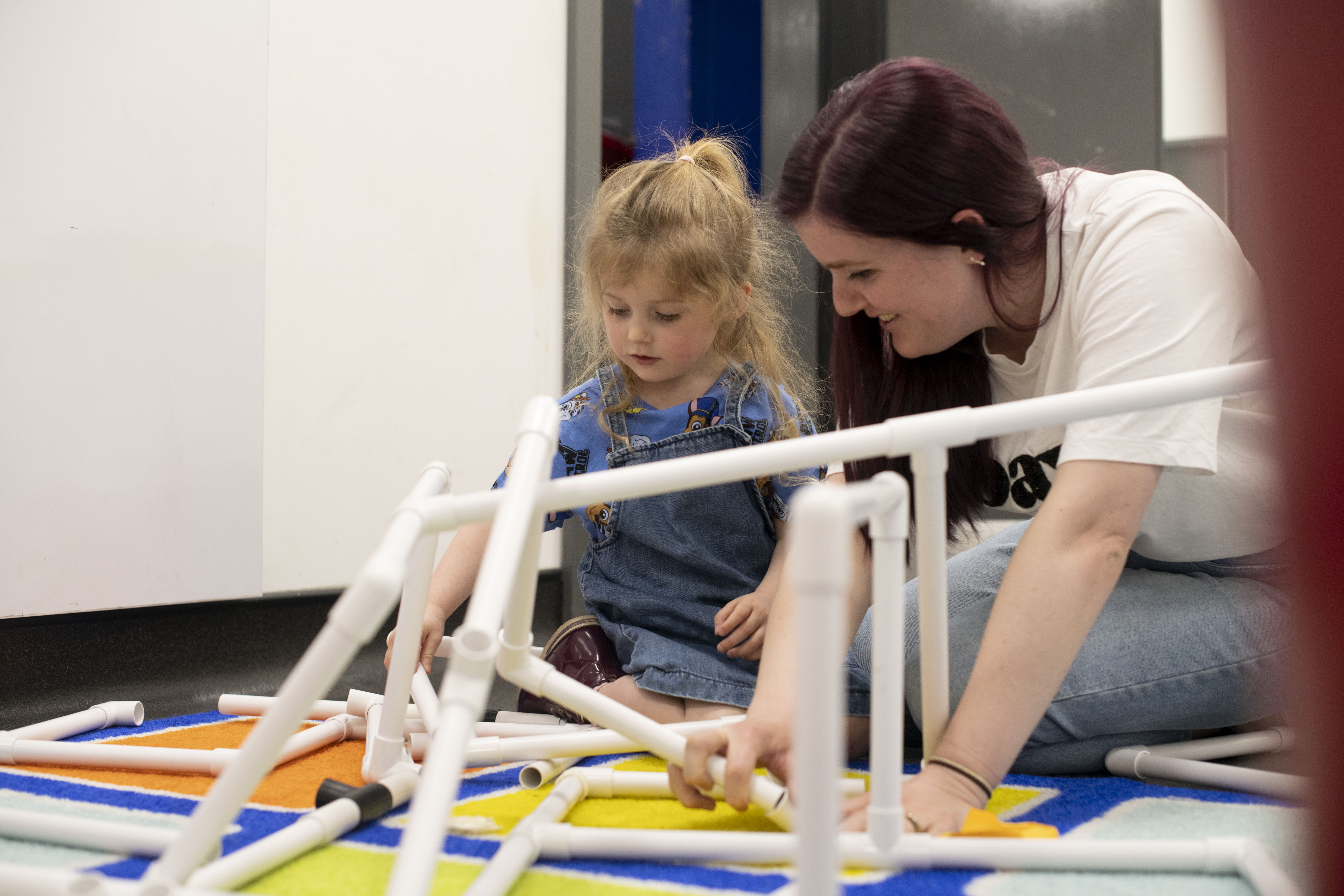A woman and a little girl are building a structure with white plastic tubing